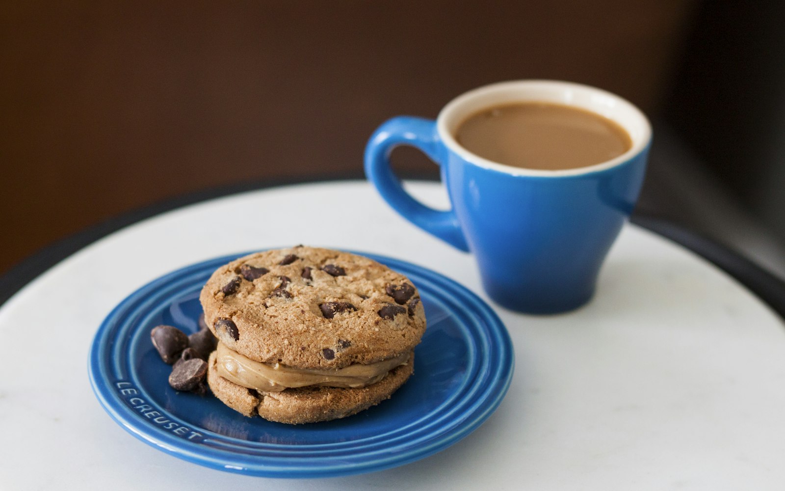 A chocolate chip cookie on a blue plate next to a cup of coffee