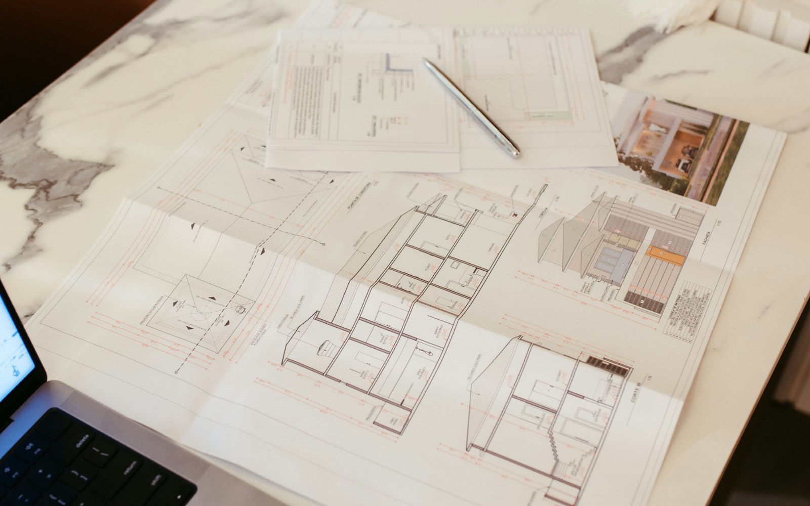 Architectural plans spread across a desk next to a laptop
